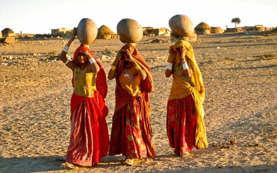 Rajasthani women in vivid saris carrying water pots through a desert village